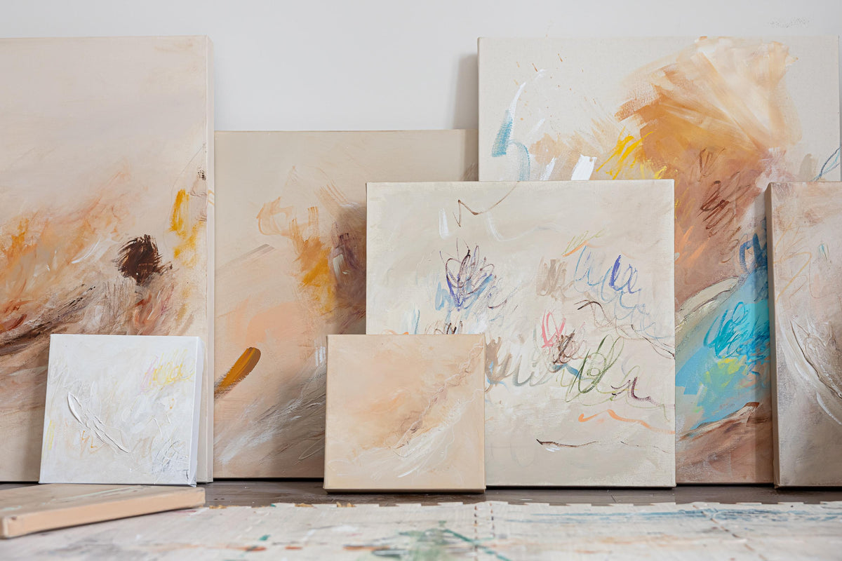 Tableaux abstraits colorés posés contre un mur, tons doux et touches de bleu, orange, beige.