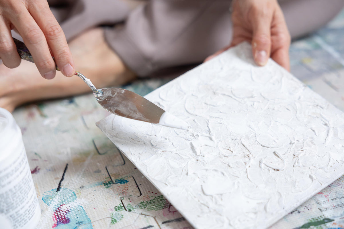 Main appliquant de la texture blanche sur une toile abstraite avec un couteau à peindre