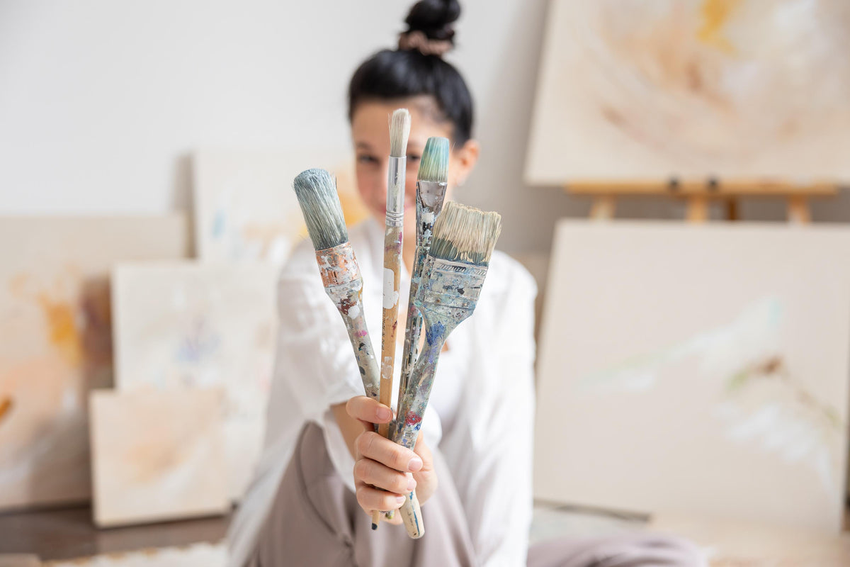 Femme artiste tenant des pinceaux devant toiles abstraites, atelier lumineux