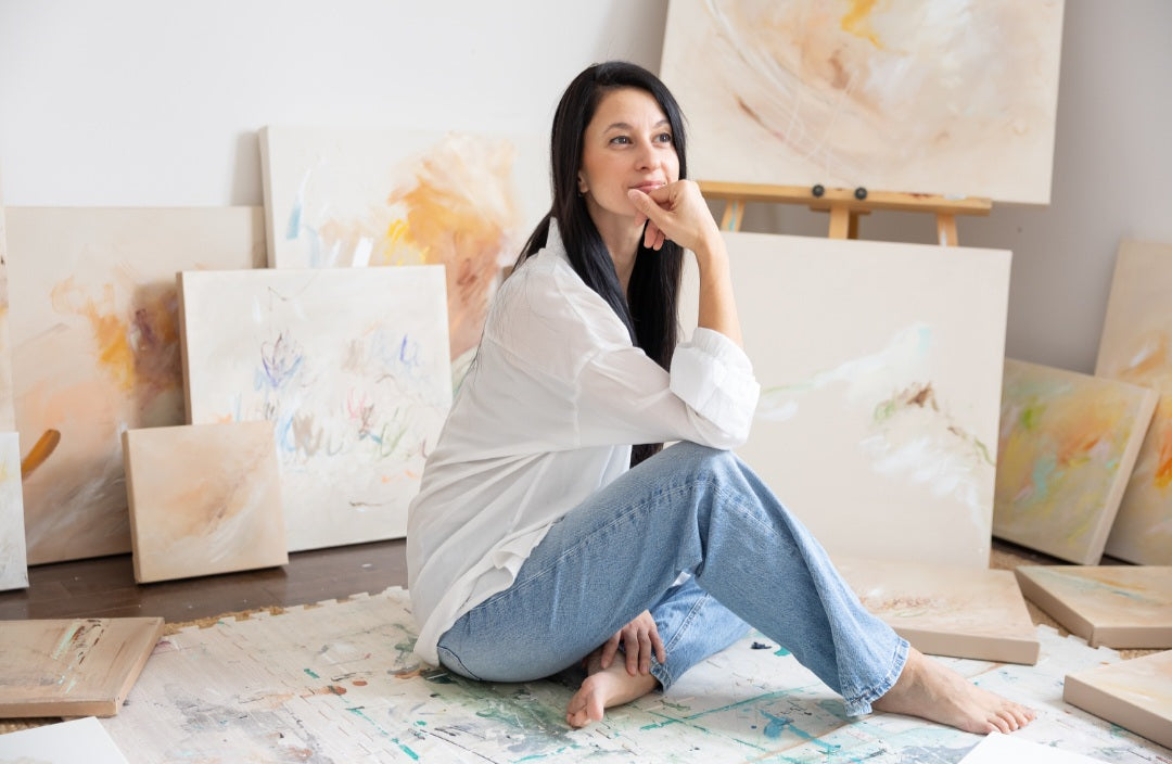 Artiste assise dans un atelier entourée de tableaux abstraits aux tons doux et pastel